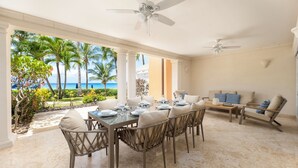 A dining area with a view of the ocean, featuring a table set for four, wicker chairs, and a sofa with patterned cushions.
