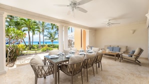 A dining area with a view of the ocean, featuring a table set for four, wicker chairs, and a sofa with patterned cushions. - Beachfront Family Retreat - Saint Peter's Bay 111 (2 bed) (Battaleys)
