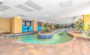 An indoor swimming pool with a tiled edge, a poolside area with lounge chairs, and a ceiling with recessed lighting.