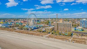Een kuststadsgezicht met een groot reuzenrad, strandhotels en een heldere blauwe lucht.