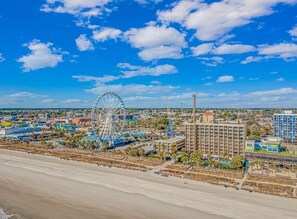 Un paisaje urbano costero con una noria grande, hoteles frente a la playa y un cielo azul despejado.