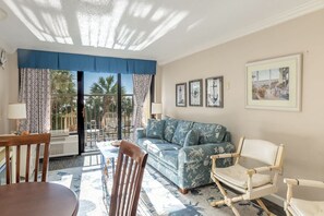 A living room with a sofa, chairs, a table, and a balcony with a view.