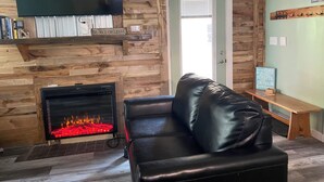 Un salon chaleureux avec une cheminée, un canapé en cuir et un téléviseur fixé au mur.