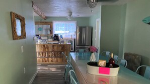 Un espace repas avec une table en verre, des chaises, un coin bar en bois et une cuisine en arrière-plan.