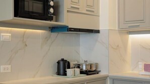 A kitchen with white cabinets, a black microwave, a coffee maker, and a kettle on the counter. - Warm and Classic Modern Room (Chiang Mai)