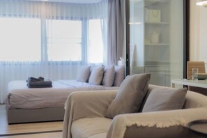 A modern hotel room with a bed, a sofa, a glass partition, and a small table with a glass. - Warm and Classic Modern Room (Chiang Mai)