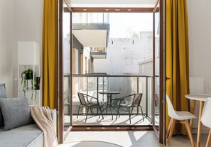 A modern living room with a sofa, a coffee table, and two chairs. There is a glass door leading to an outdoor area with a table and chairs.