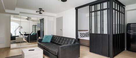 Un salón moderno con un sofá de cuero negro, una mesa de centro de madera clara y un separador negro.