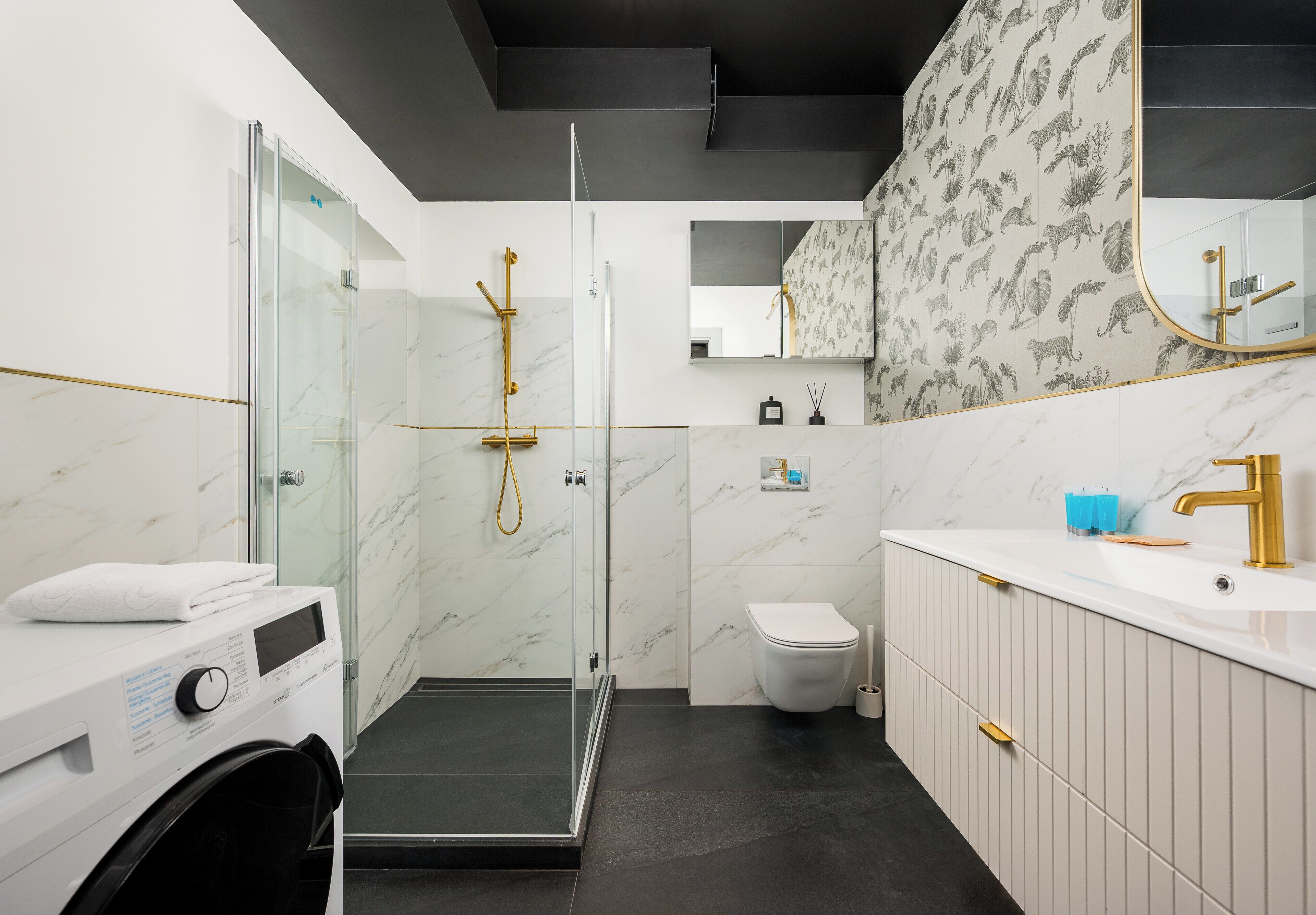A modern bathroom with a glass-enclosed shower, a white toilet, and a vanity with a gold faucet.