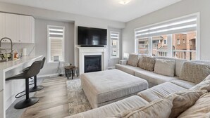 En moderne stue med pejs, sofa, spiseplads med barstole og et fjernsyn.