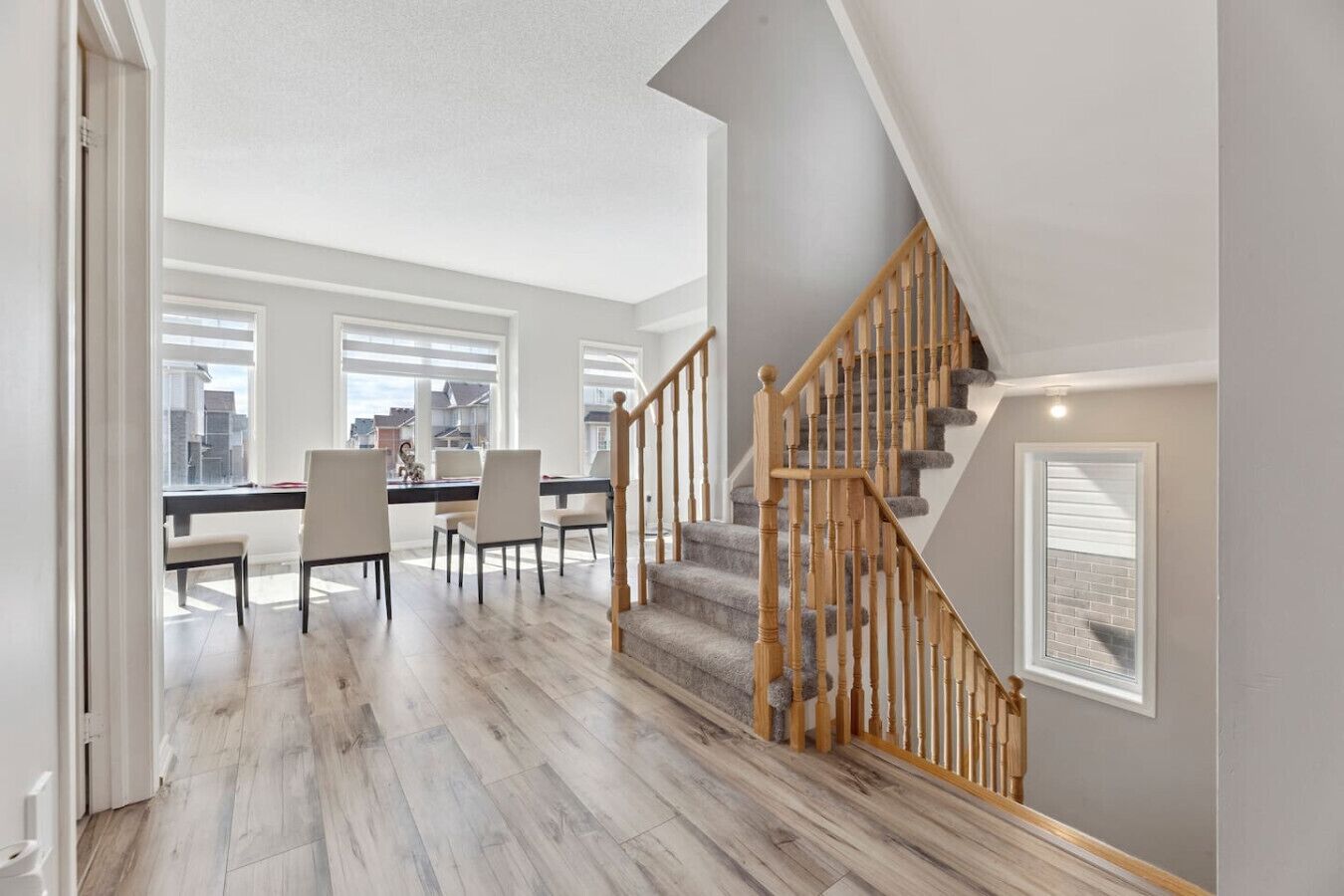 A spacious living area with a dining table, chairs, and a staircase with wooden railings.