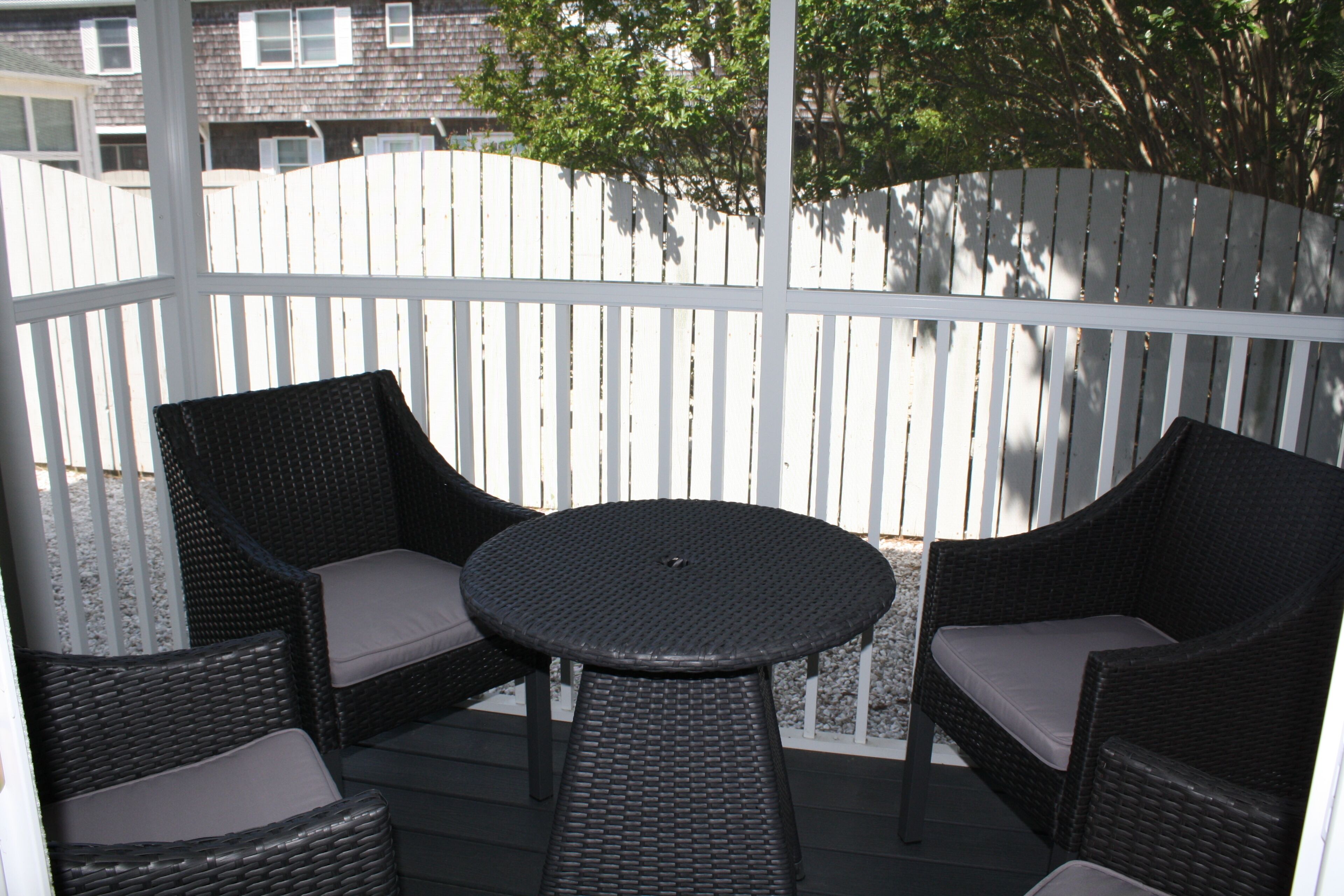 Eine überdachte Terrasse mit Korbmöbeln und einem weißen Zaun.