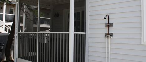 A covered porch with a railing, a window, and a wall-mounted shower.