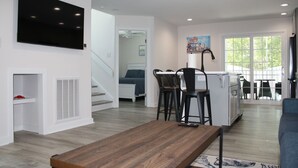 Un salon moderne doté d’un téléviseur à écran plat, d’un coin repas avec un îlot de cuisine, d’un escalier et d’une grande fenêtre.