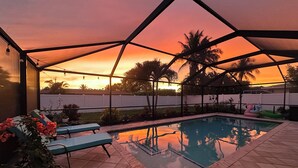 Una piscina scoperta coperta con lettini, una pianta in vaso e vista sul tramonto.
