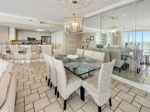 A dining area with a glass table and wicker chairs, a kitchen with white cabinets, and a large mirror reflecting the room. - 7th Heaven 4 bed / 4 bath at Belle Mer (Navarre Beach)