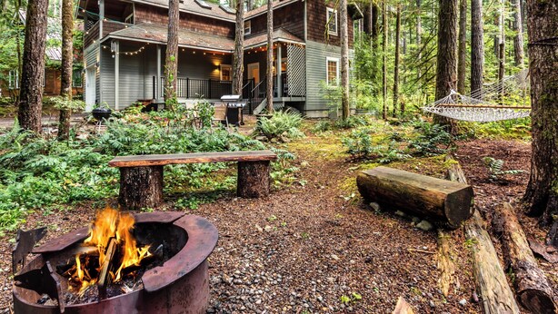 A cabin in a forest with a fire pit, outdoor seating, and a hammock.