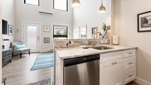 A modern kitchen with a dishwasher, white cabinets, and a large window.