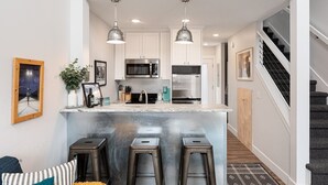 A modern kitchen with white cabinets, stainless steel appliances, and a bar area with stools.