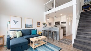 A modern living room with a sectional sofa, a coffee table, and a kitchen area visible through an open door.
