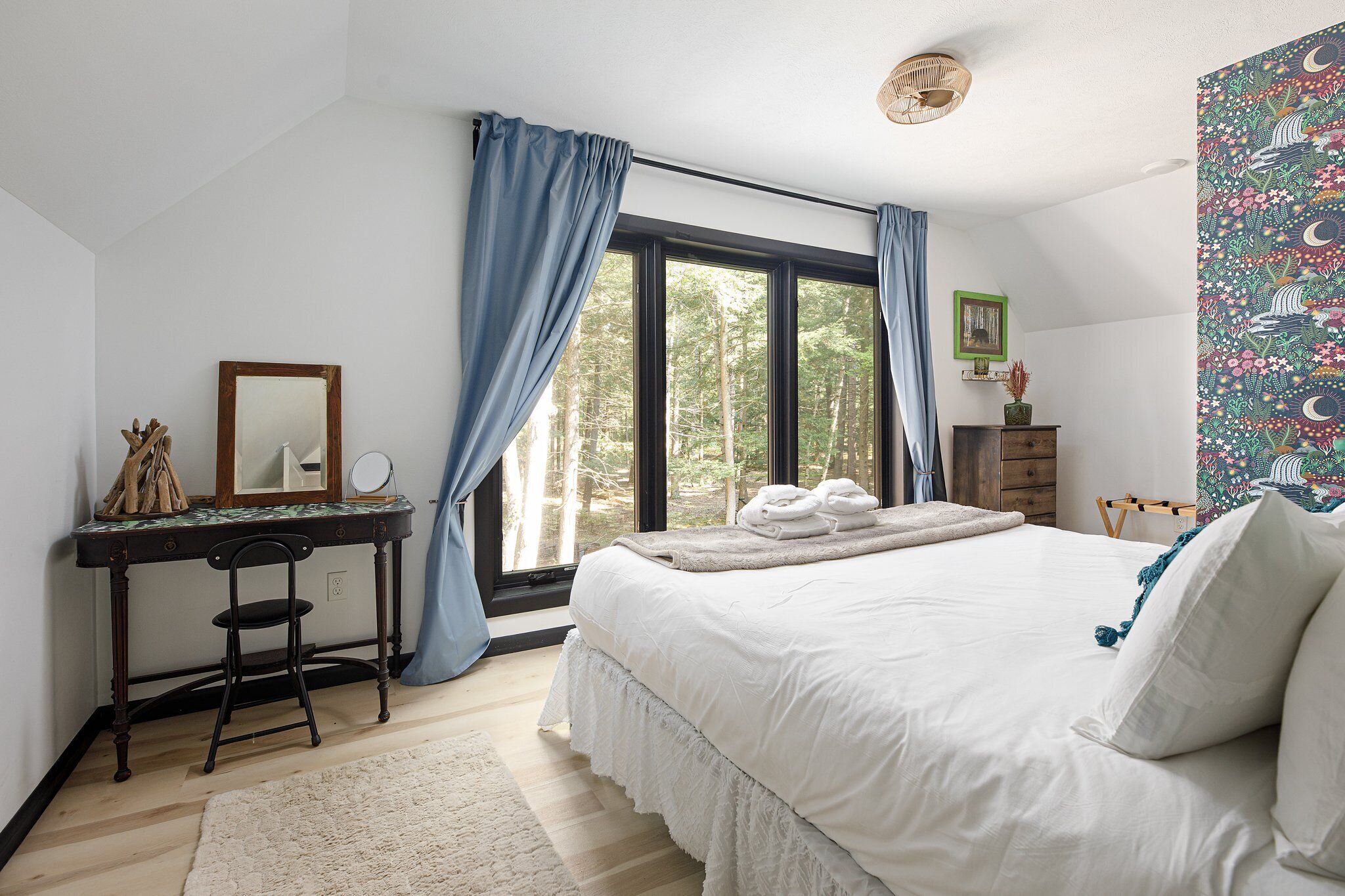 Un dormitorio con una cama grande, un escritorio con silla, una ventana con cortinas y un tapiz en la pared.