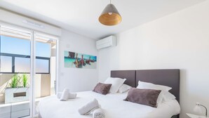 A modern hotel room with a large bed, a view of boats through a sliding door, a painting on the wall, and a ceiling fan.