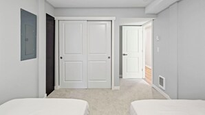 Quarto com duas camas, uma porta branca e um corredor que dá para outro cômodo.