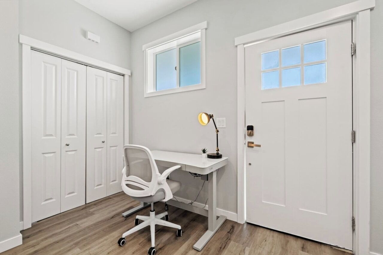 A room with a white desk, a white office chair, a lamp, and a door with a window.