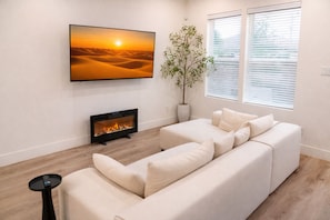 A living room with a large flat-screen TV, a fireplace, a sofa, and a potted plant. - Stylish & Spacious 3BR Gem W/ Hottub Near Downtown (Houston)