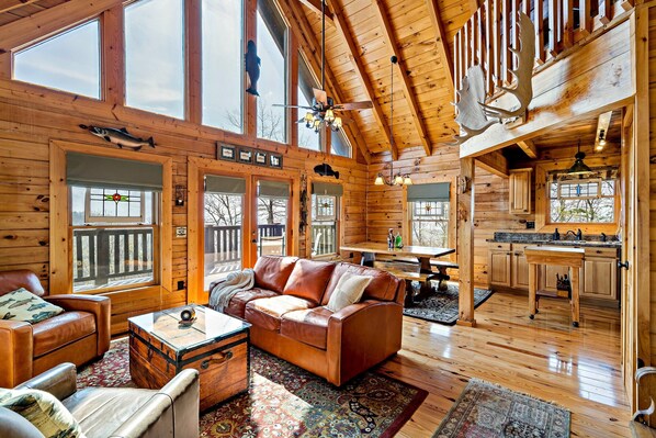 A spacious cabin with a wooden interior, a leather sofa, a dining area, and a kitchen.