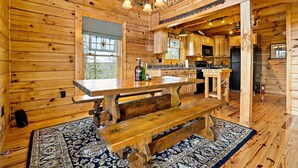 A wooden cabin interior with a dining area, kitchen, and a large window. - Nice Views, Log Cabin, Gated Community - Mountain Vista by Carolina Properties (Bostic)