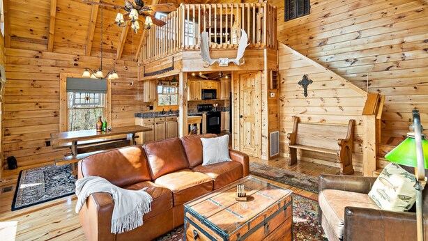 A wooden cabin interior with a loft bedroom, a dining area, and a living room furnished with leather sofas and a coffee table. - Nice Views, Log Cabin, Gated Community - Mountain Vista by Carolina Properties (Bostic)