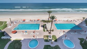 Un resort con dos piscinas, zonas de descanso en la playa y vistas al océano.