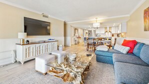 Un salón amplio con una mesa de centro de vidrio, un sofá azul y un mueble blanco para el equipo de entretenimiento.