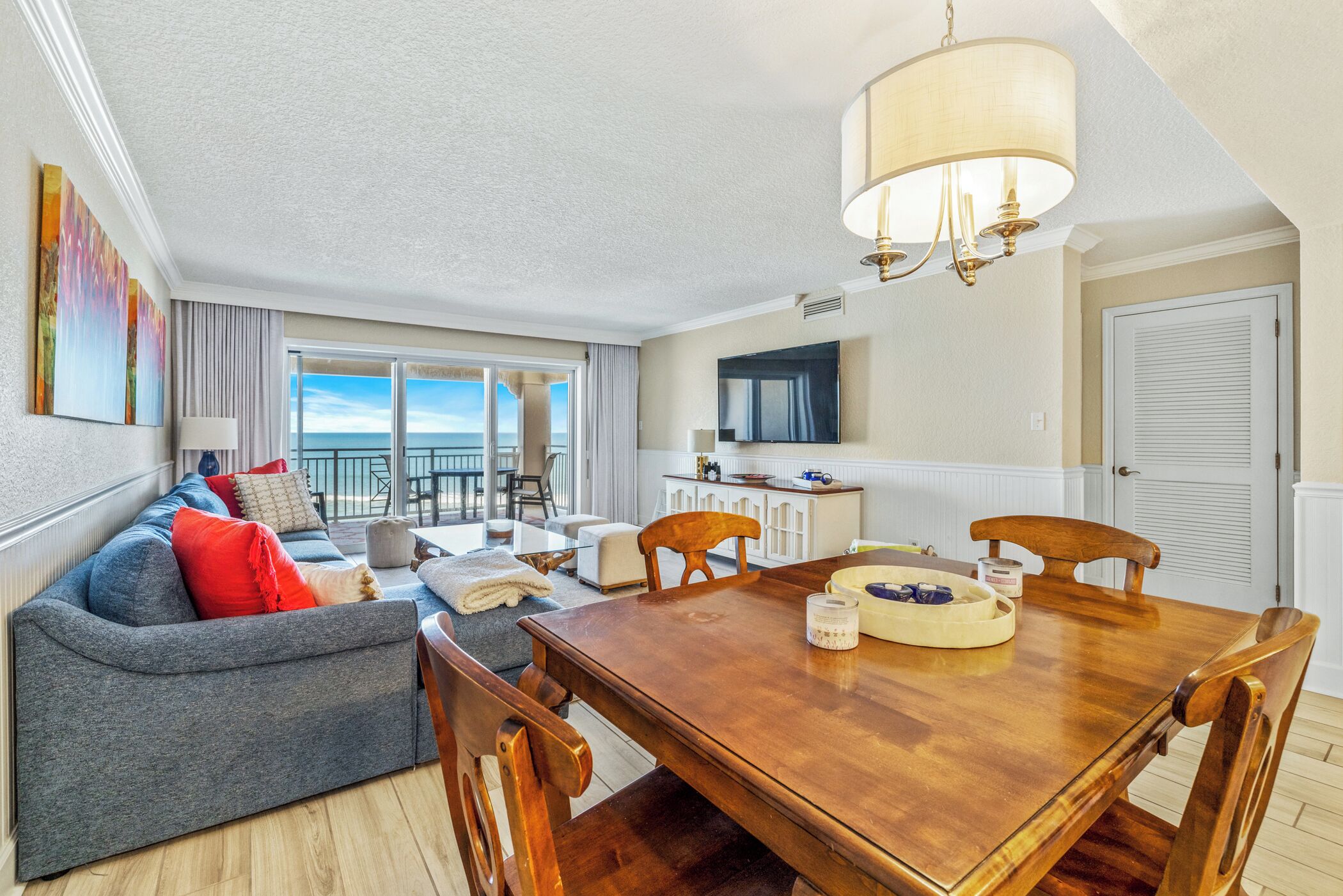 A modern living room with a grey sofa, wooden dining table, and a view of the ocean.