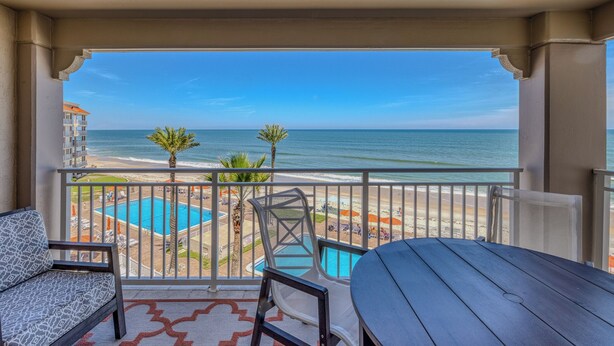 Un balcón con vista al océano, una piscina y sillas de playa.