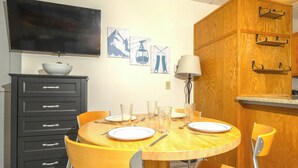 A dining area with a round wooden table, four chairs, and a TV mounted on the wall. - Ski-in, Ski-out Studio Condo at Smugglers' Notch Resort (Cambridge)