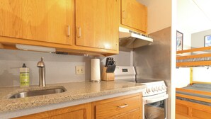 A kitchen with wooden cabinets, a stainless steel sink, a stove, and a window overlooking a bunk bed area. - Ski-in, Ski-out Studio Condo at Smugglers' Notch Resort (Cambridge)