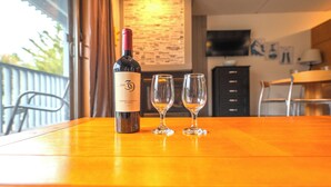 A bottle of wine and two glasses on a wooden table in a room with a TV and a bulletin board in the background. - Ski-in, Ski-out Studio Condo at Smugglers' Notch Resort (Cambridge)