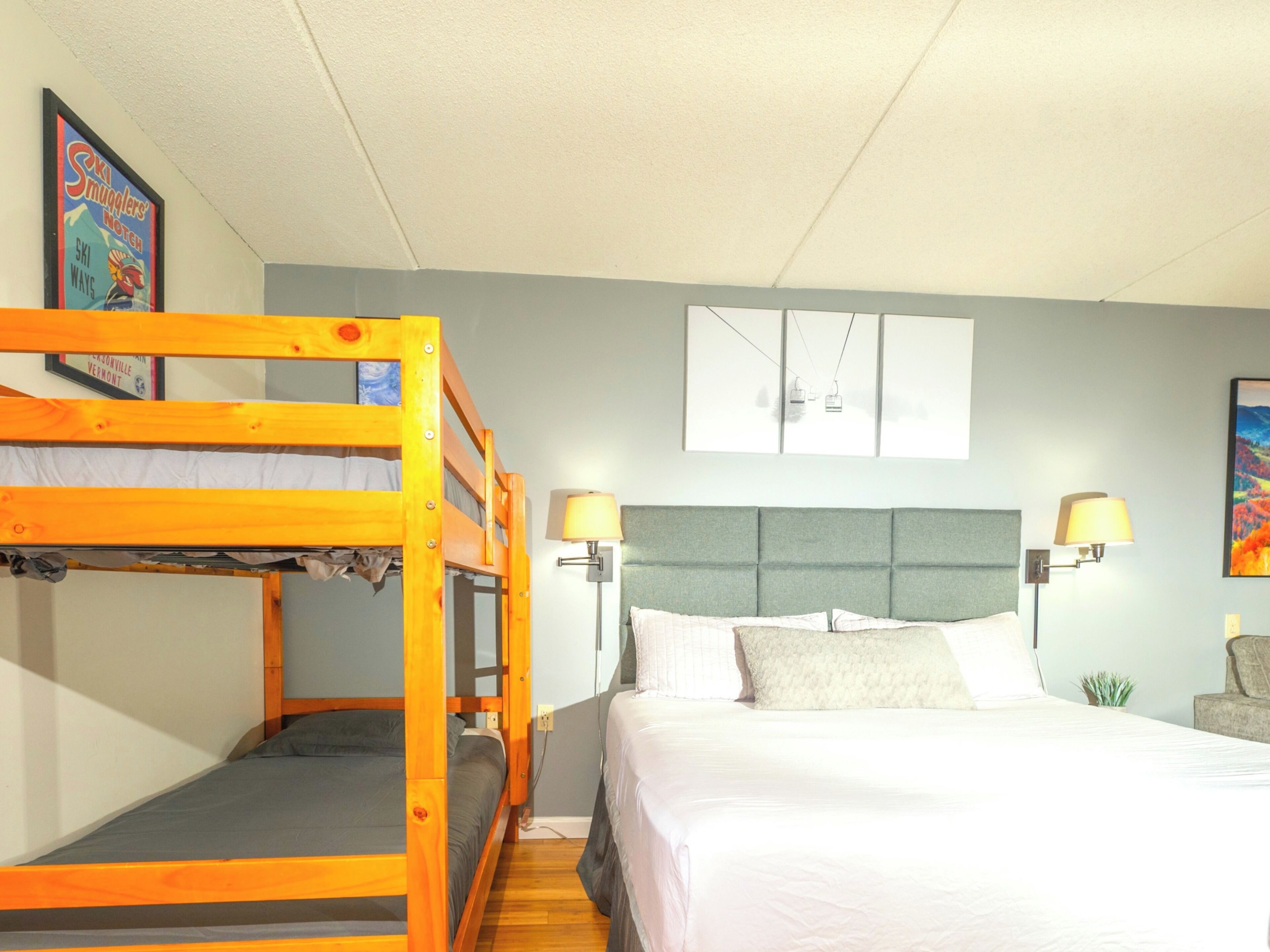 A room with bunk beds, a bed with pillows, a wall-mounted lamp, and a framed picture.