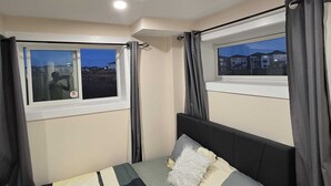Un dormitorio con una cama, dos ventanas y vistas a edificios.