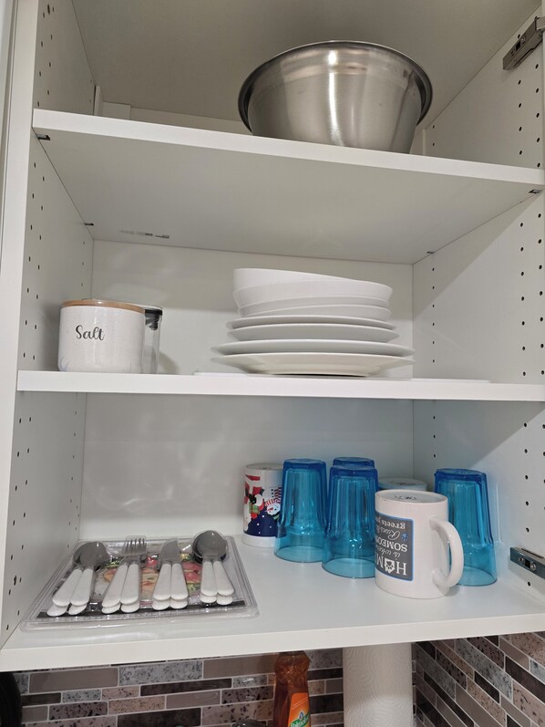 Un garde-manger de cuisine avec des étagères contenant un récipient à sel, des assiettes, des tasses bleues et des ustensiles de cuisine.