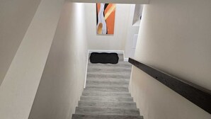 Una escalera con acabado de madera, paredes blancas y barandal negro.