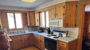 A kitchen with wooden cabinets, a microwave, a stove, and a sink. - Cozy 3-bedroom home Brownington, VT-On VASA Trails - Near Lake Willoughby (Brownington)