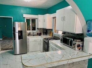 A kitchen with white cabinets, a stainless steel refrigerator, a microwave, a stove, and a water dispenser.