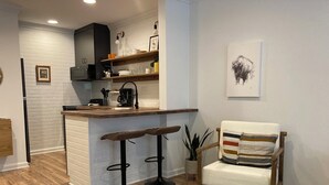 Eine moderne Küche mit einer zentralen Kochinsel, zwei Barhocker, einem Holzhocker und einem Kuhfellteppich.