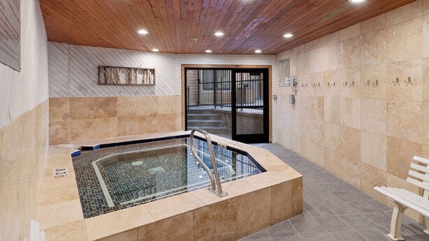 A modern indoor pool area with a wooden ceiling, tiled walls, and a glass-enclosed hot tub. - Carriage House 101 | Kitchenette | Near Dining & Shopping | Hot Tub | Pool (Park City)