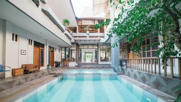 An indoor swimming pool with a view of the building's interior, including a staircase and seating area. - Blok O International Guest House by MHM (Banguntapan)