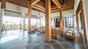 A spacious indoor area with wooden pillars, tiled flooring, and several wooden chairs. - Blok O International Guest House by MHM (Banguntapan)
