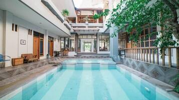 Una piscina con escalones de acceso, rodeada por un edificio con balcón y zona de estar interior.